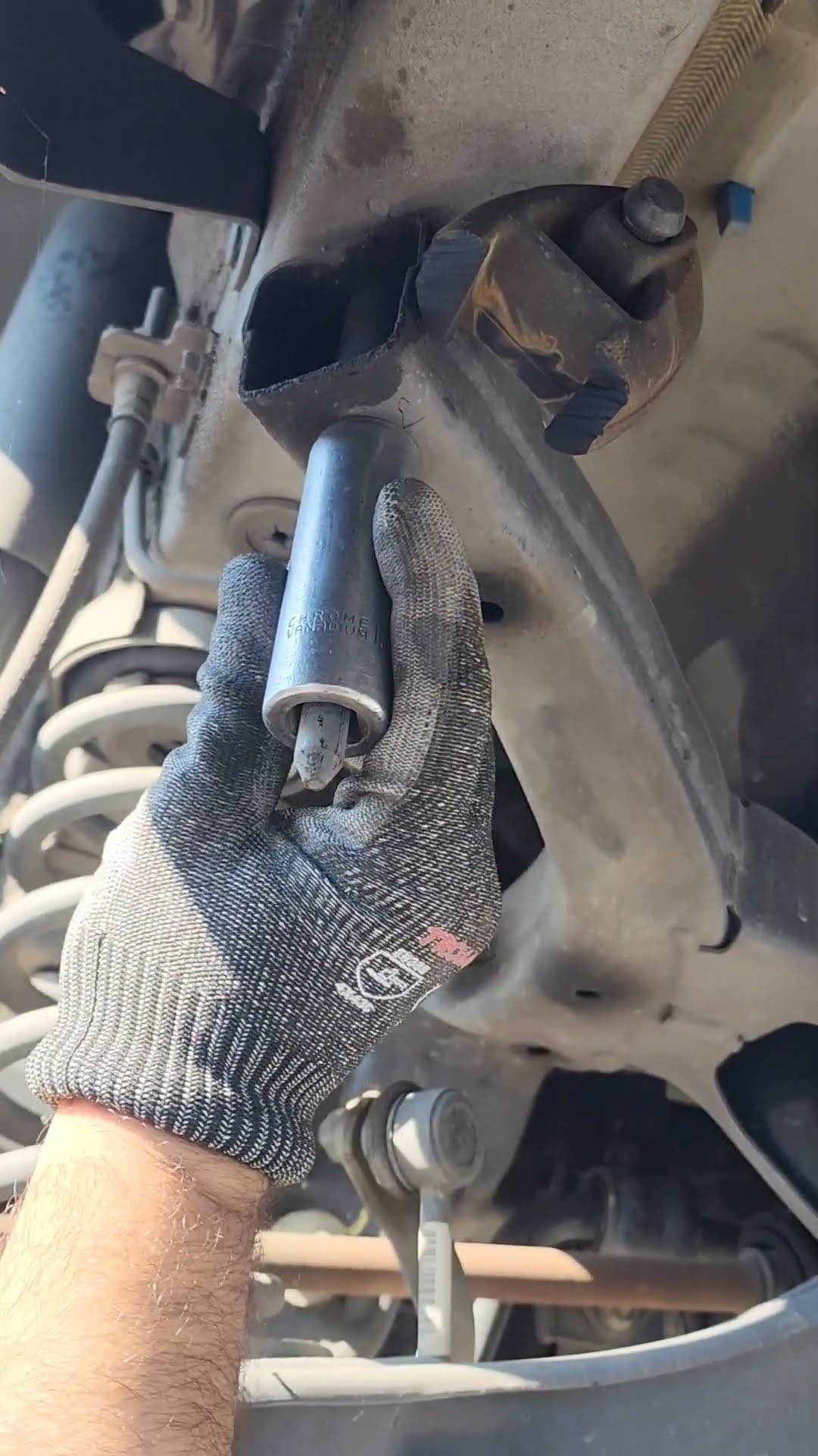 A gloved hand holding a socket below a suspension mounting point.